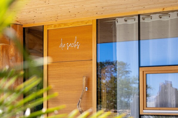 A modern interior with wooden cabinetry, a glass door with a handle, and a window reflecting an outdoor scene.