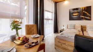 Ett modernt hotellrum med ett träpanelat tak, en säng med mönstrade kuddar, ett matbord med frukt och en vas med blommor samt en stor, abstrakt målning på väggen.
