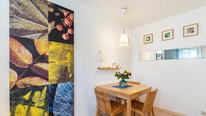 A dining area with a wooden table and wicker chairs, a wall-mounted shelf with decorative items, and a large leaf-patterned artwork. - "Am Paradies" Apartment – Relaxation in Baden-Baden (Baden-Baden)