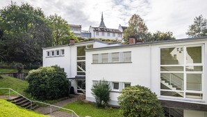 A modern two-story building with a staircase leading to the upper floor, surrounded by greenery and a church in the background. - "Am Paradies" Apartment – Relaxation in Baden-Baden (Baden-Baden)