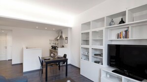 Ein modernes Wohnzimmer mit Essbereich, einer Küche und einem Fernseher auf einem weißen Regal.