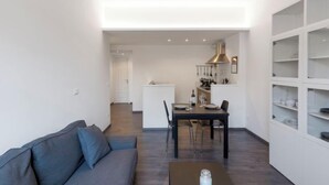 Ein modernes Wohnzimmer mit einer Couch, einem Esstisch und einer Küche im Hintergrund.