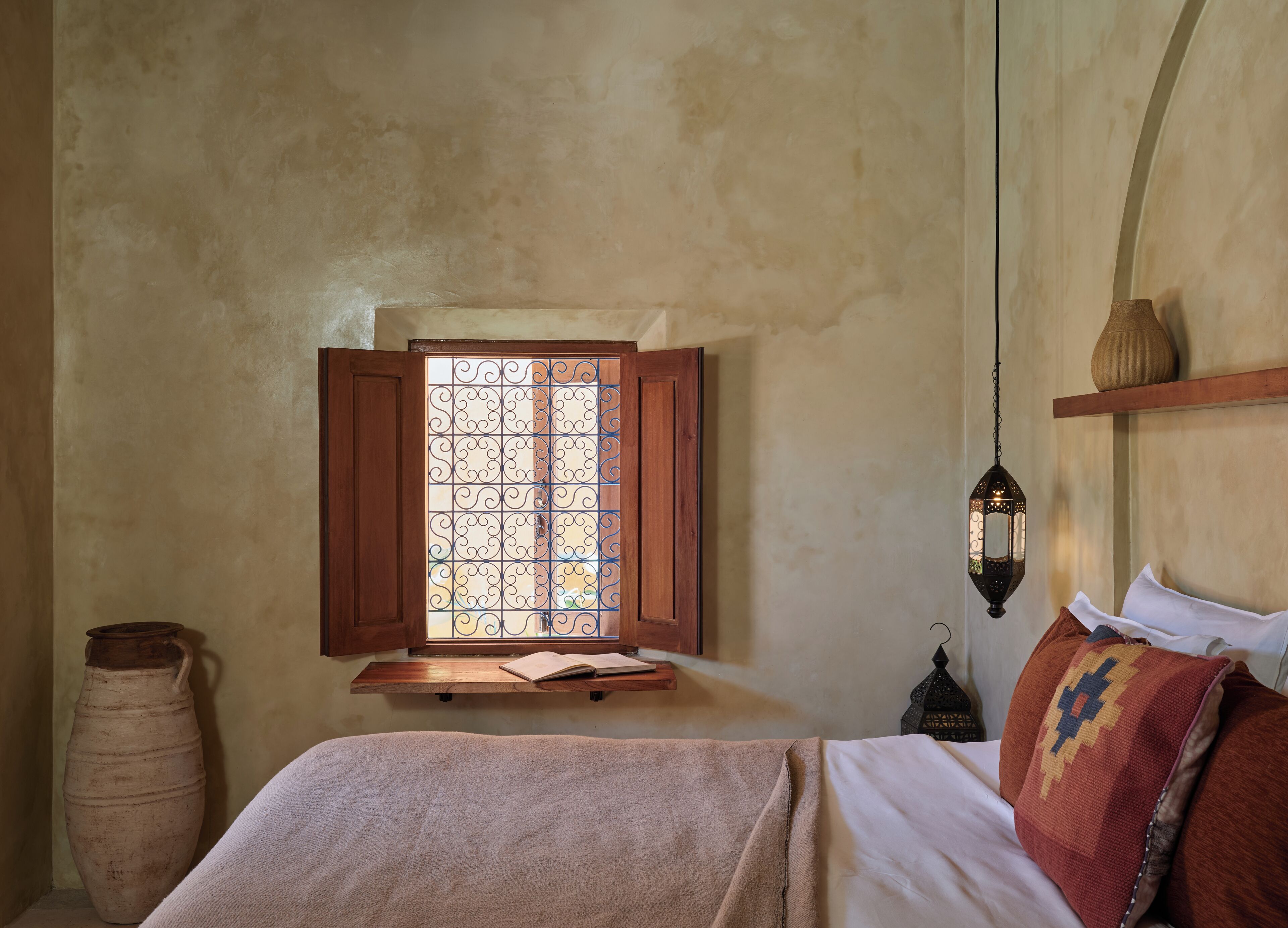 A bedroom with a window, a bedside table, a lamp, and a bed.
