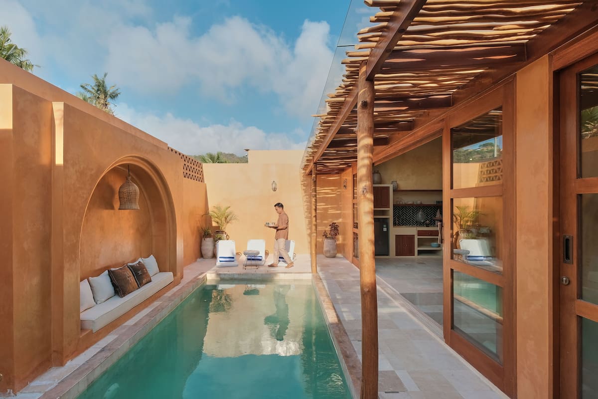 Ein Poolbereich mit einer Holzpergola, einer Sitzgruppe mit Kissen und Blick zum Himmel.