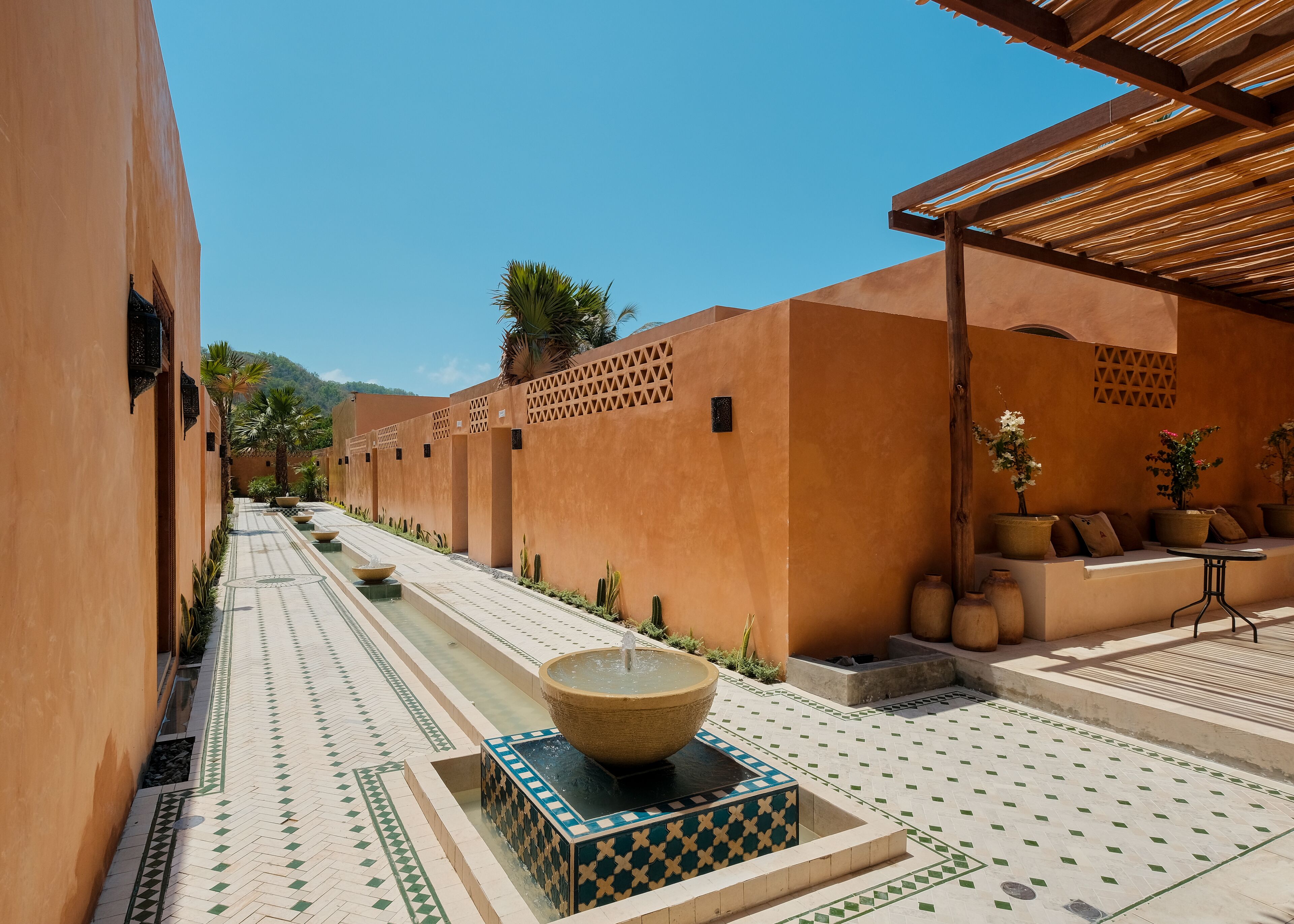 A corridor with a central water feature, patterned flooring, and a seating area with planters.