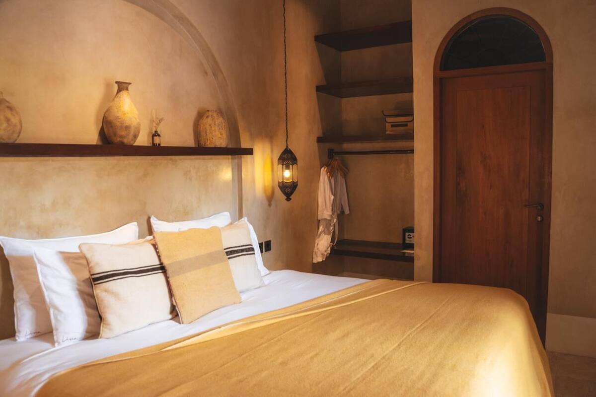 Ein Schlafzimmer mit einem Bett, Kissen, einem Regal mit Dekoration, einer hängenden Laterne und einer Holztür.