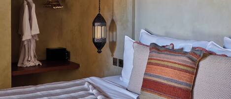 A bedroom with a bed, a hanging lantern, wooden shelves, and a small vase.