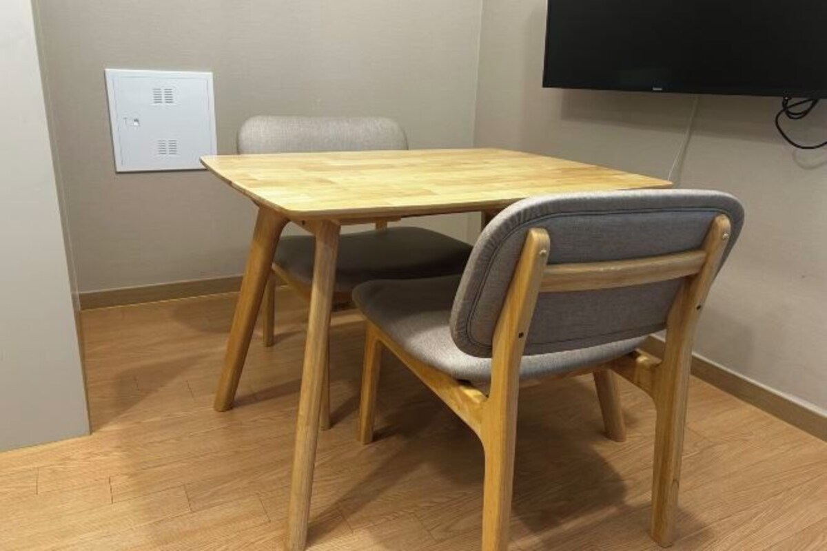 A room with a wooden table and two chairs, a television mounted on the wall, and a power outlet on the wall.