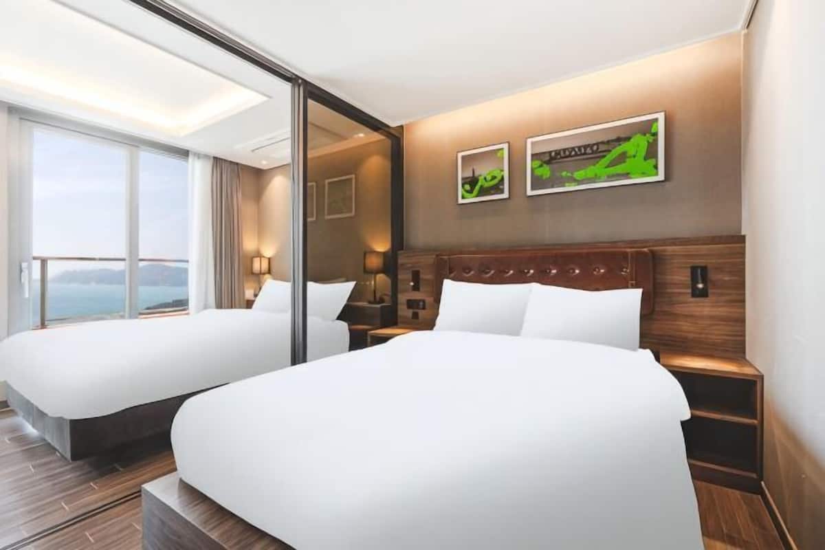 Ein Hotelzimmer mit zwei Betten, einem großen Fenster, einem Holzkopfende und Meerblick.