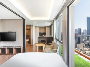 Una habitación de hotel moderna con una cama grande, televisión, zona de comedor y vistas a la ciudad.