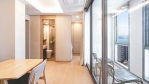 A modern apartment with a wooden dining table, a small kitchenette, and a balcony with a city view.