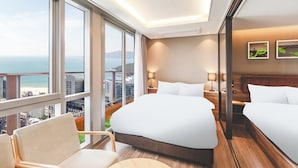 A hotel room with a large bed, a chair, and a view of the city and sea.