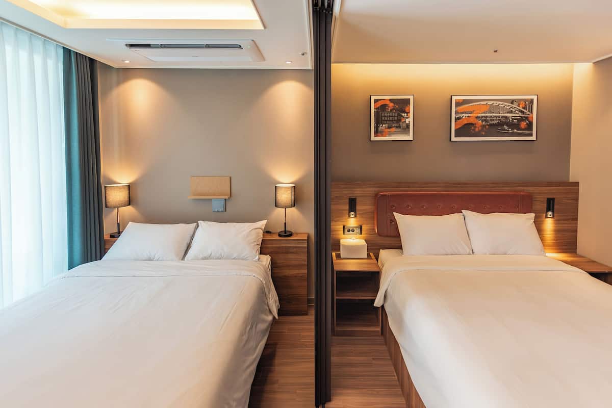 Ein Hotelzimmer mit zwei Betten, einem Nachttisch mit Lampe, einem Wandbild und einem Fenster mit Vorhängen.