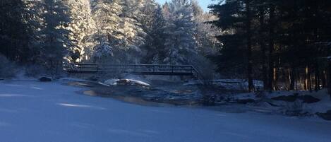 A snow-covered landscape with a bridge and dense trees.