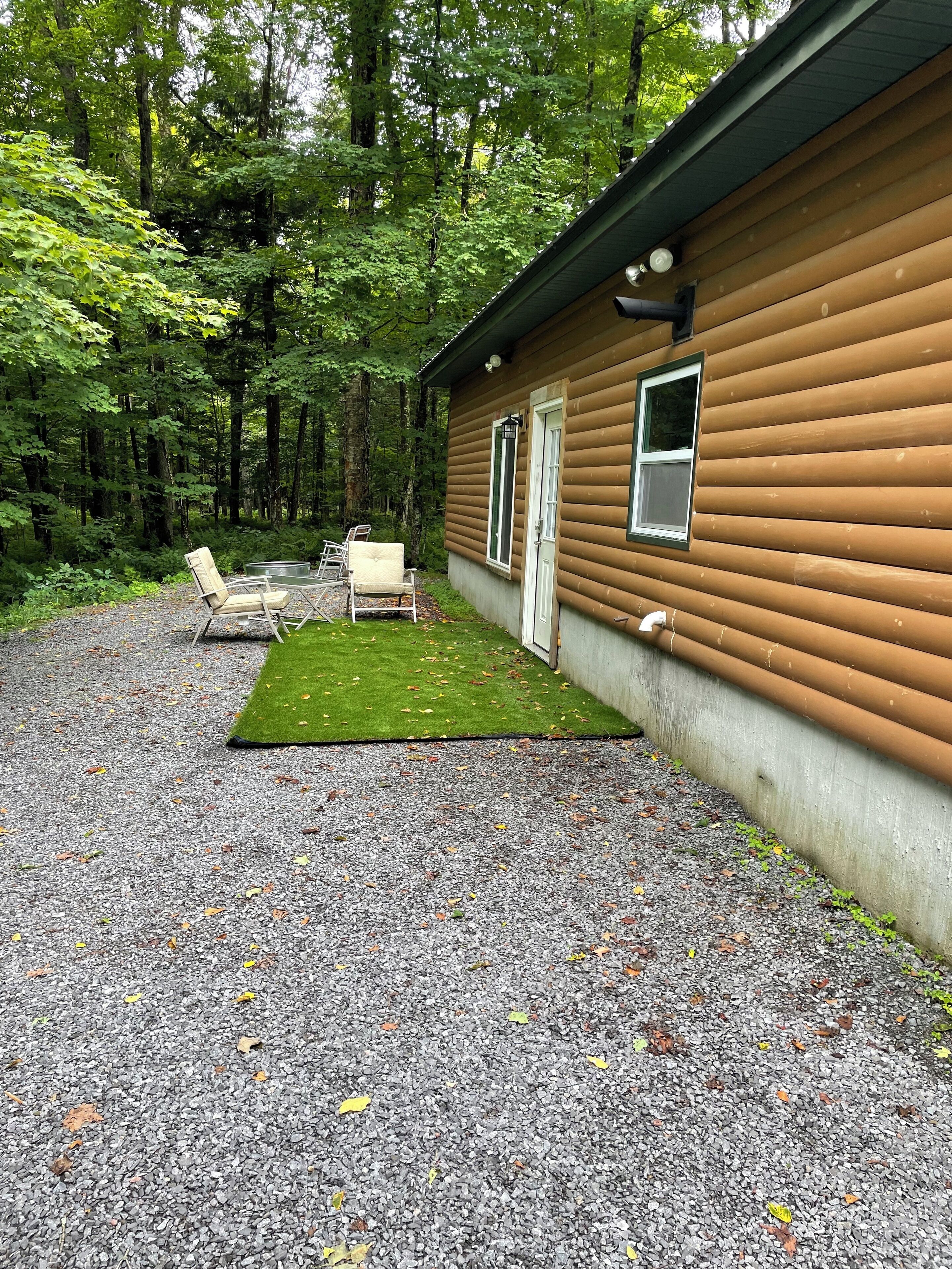 A cabin with a gravel driveway, a grassy area, and two chairs.