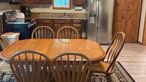 Een keuken met houten kastjes, een roestvrijstalen koelkast, een magnetron, een fornuis en een eettafel met stoelen.