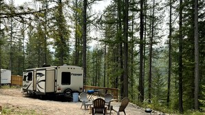 Ein Campingplatz mit einem Wohnwagen mit dem Aufdruck 'Premier' und einer Terrasse mit Stühlen und Grill.