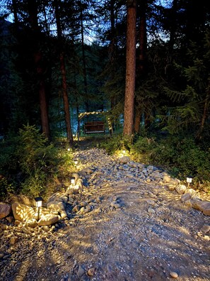 A forest path with a wooden bench and string lights, surrounded by rocks and trees.