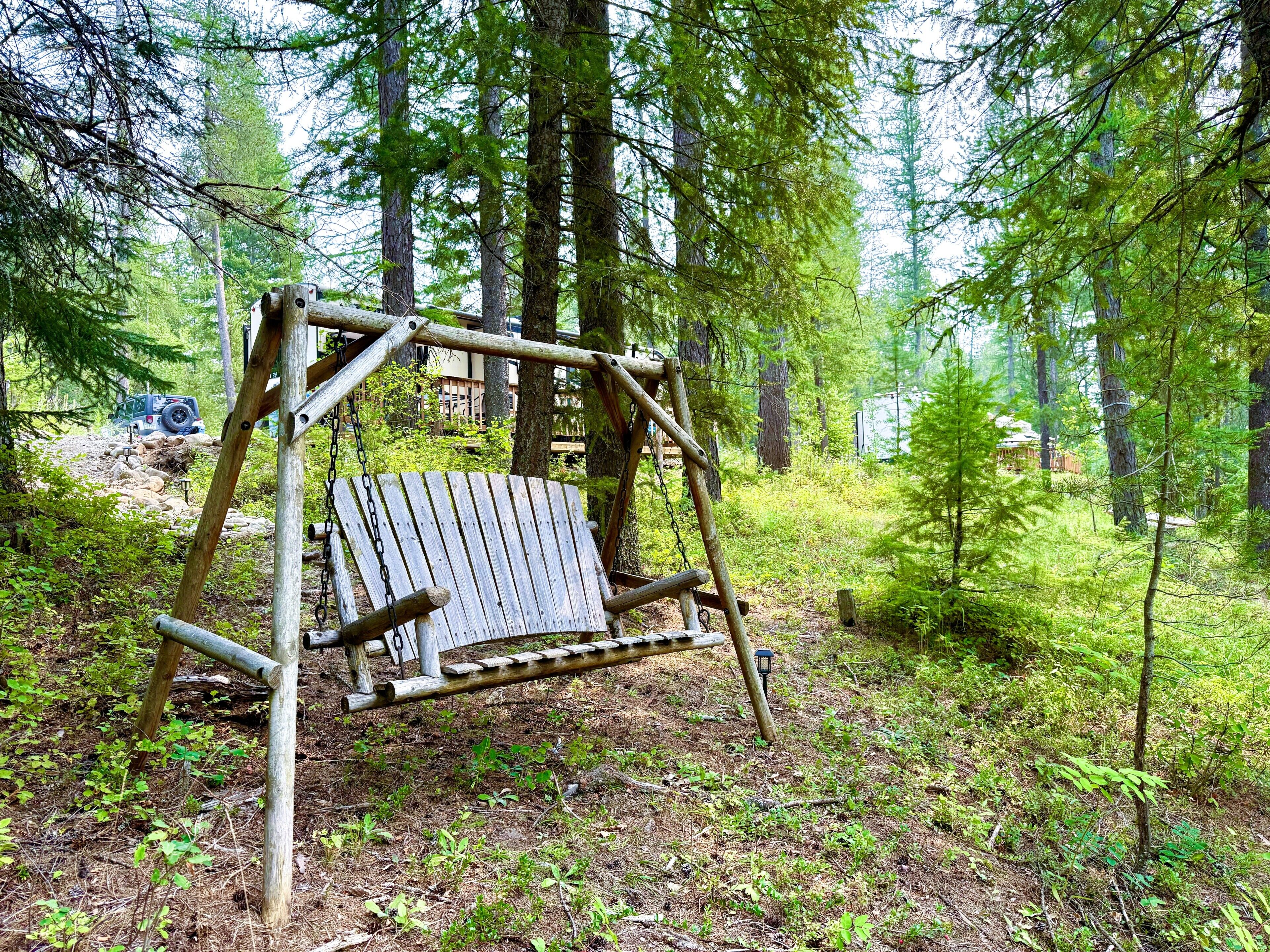 Un ensemble de balançoires en bois installé dans une zone boisée, avec un véhicule garé à proximité.