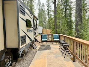 An RV with 'PREMIER' branding, a deck with outdoor furniture, and a forested backdrop.