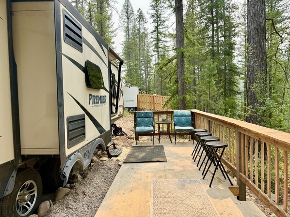 An RV with 'PREMIER' branding, a deck with outdoor furniture, and a forested backdrop.