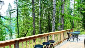 Eine Holzterrasse mit Geländer, Sitzgelegenheiten und Blick auf einen Wald.
