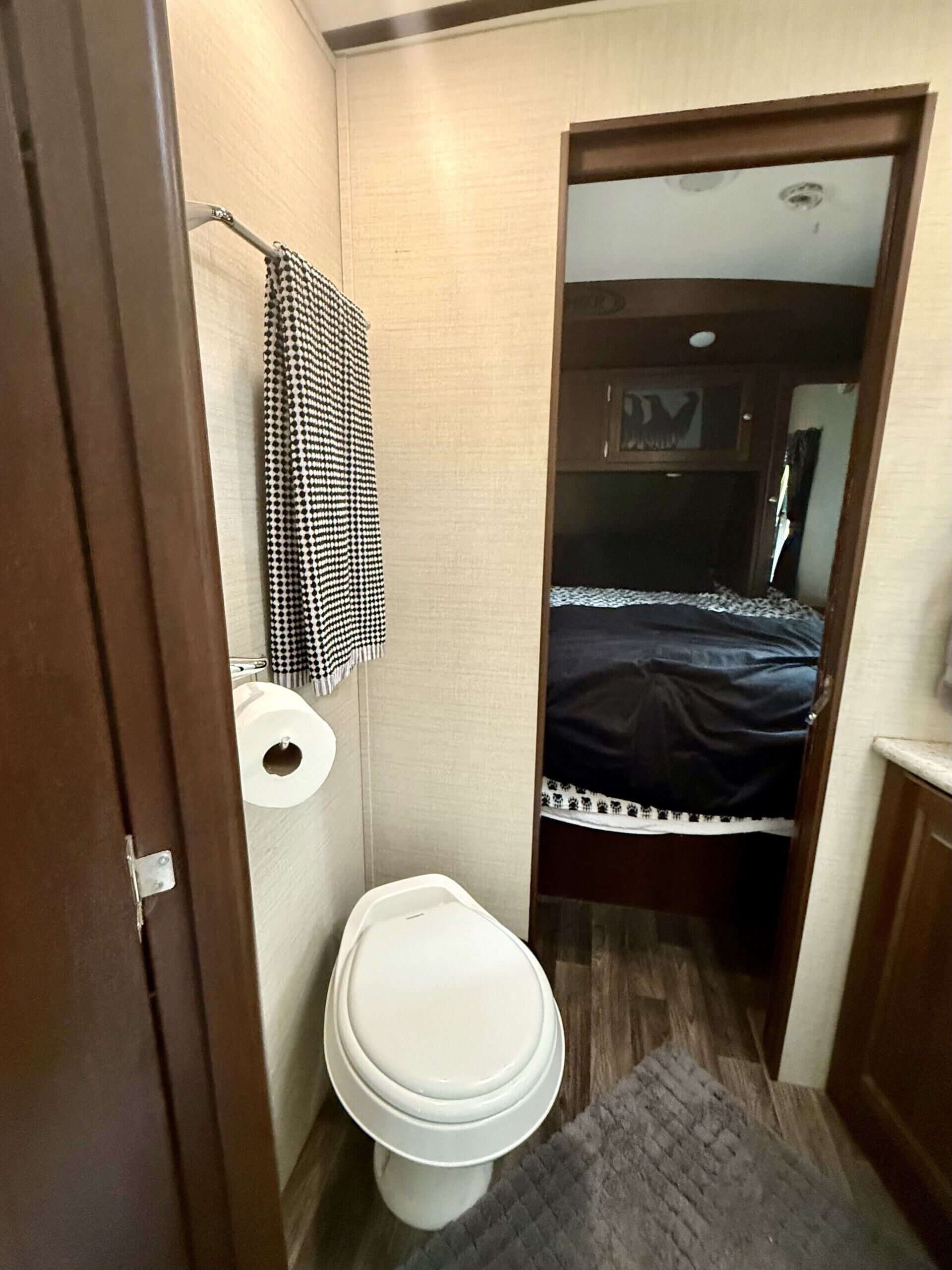 Une petite salle de bain comprenant des toilettes, une serviette suspendue à un porte-serviettes, et un lit dans la pièce adjacente.