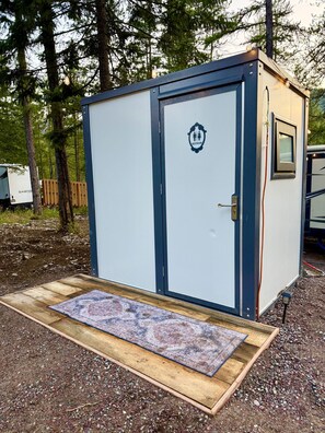 A portable restroom with a door, a window, and a small rug in front.