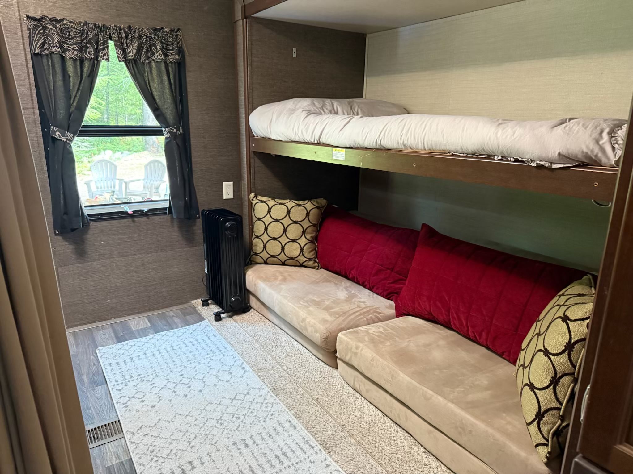A compact RV interior with a bunk bed, a sofa, and a window with curtains.