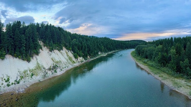 Ein Fluss, der von dichtem Wald und einer steilen, felsigen Klippe gesäumt wird.