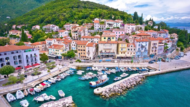 Une ville côtière aux bâtiments aux couleurs vives, un port de plaisance avec des bateaux et une digue rocheuse.