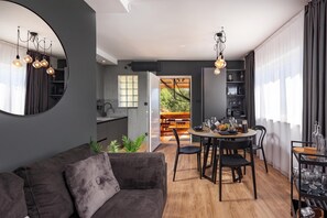 A modern living room with a dark grey sofa, a dining area with a wooden table and chairs, and a kitchen in the background.