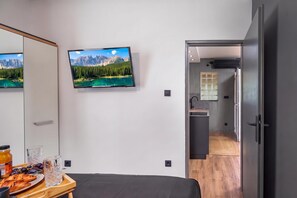 Une chambre moderne avec un lit, un téléviseur diffusant un paysage de montagne et un plateau de petit-déjeuner avec des œufs et du pain.