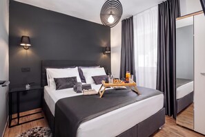 Et moderne soveværelse med en stor seng, sengeborde, en sengetavle, et bakke med morgenmadsprodukter og et stort spejl.