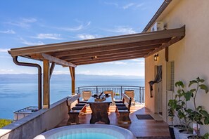 An outdoor terrace with a pool, wooden furniture, and a view of the sea.