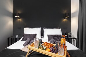 A neatly made bed with a tray of breakfast items including croissants, fruit, and a bottle of orange juice.
