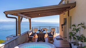 Une terrasse avec une table et des chaises, un jacuzzi et une vue sur la mer.