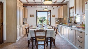 A spacious kitchen with wooden cabinets, a dining table set for six, and a view through the window.