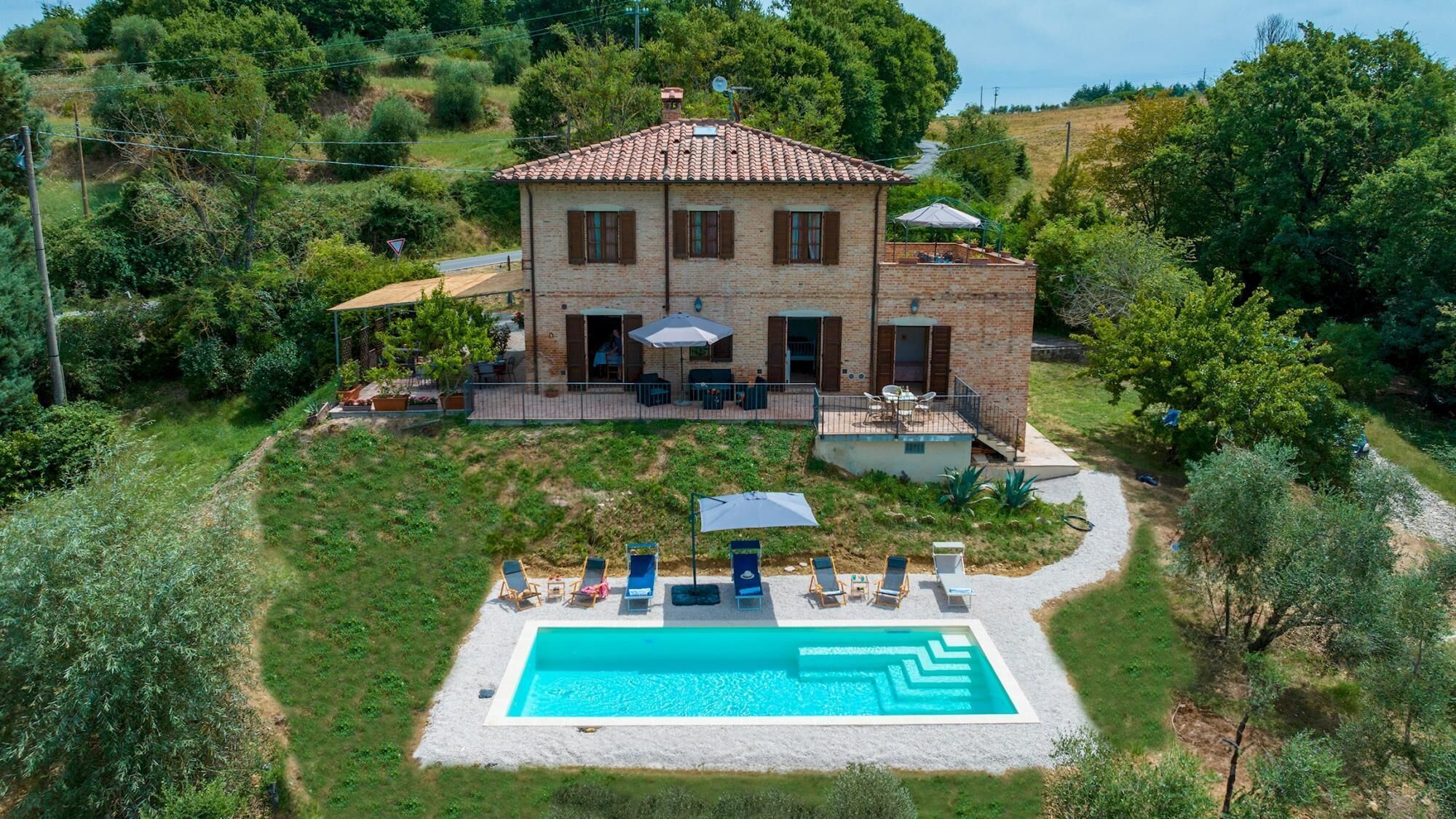 Una casa de dos pisos con piscina, rodeada de vegetación.