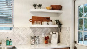 A kitchen with white herringbone tile backsplash, a coffee maker, and a wooden cutting board on a shelf. - Scenic Oasis: King Bed Suite & Panoramic Views & Ultra Fast Fiber WiFi  (SAN DIEGO)