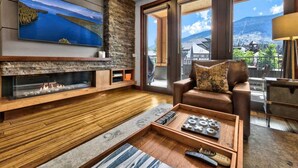 A modern living room with a fireplace, a large TV, a sofa, and a view of mountains through large windows. - Luxury @Heavenly, Pool, Hot Tub, 6 Beds, Game Room (South Lake Tahoe)