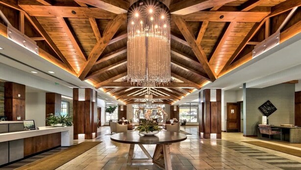 A spacious lobby with a high ceiling, wooden beams, a central chandelier, and a reception desk. - Luxury @Heavenly, Pool, Hot Tub, 6 Beds, Game Room (South Lake Tahoe)
