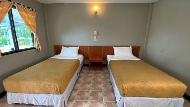 A room with two beds, a small table, a wall-mounted light, and a window with curtains. - Orchard House Resort (Ko Pha-ngan)