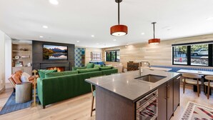 A modern kitchen with a central island, a dining area with a table and chairs, a green sofa, and a fireplace. - Mountain Nirvana| Hot Tub | Walk to Ski & Main St. (Park City)