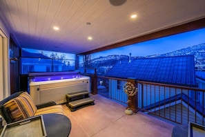 A balcony with a hot tub, seating area, and a view of a snowy landscape.