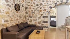 A living room with a stone wall, a brown sofa, a wooden coffee table, and a staircase leading to another room. - Stoney Villa Koxari By Estia (Hersonissos)