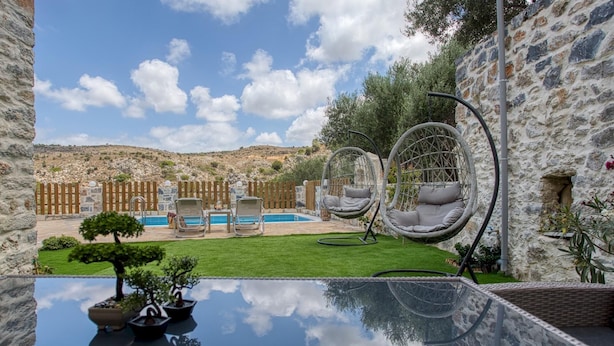 A pool area with two lounge chairs, a hanging chair, and a glass table reflecting the sky. - Stoney Villa Koxari By Estia (Hersonissos)