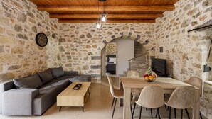 A cozy room with a stone wall, a wooden ceiling, a sofa, a dining table with chairs, and a staircase leading to another room. - Stoney Villa Koxari By Estia (Hersonissos)