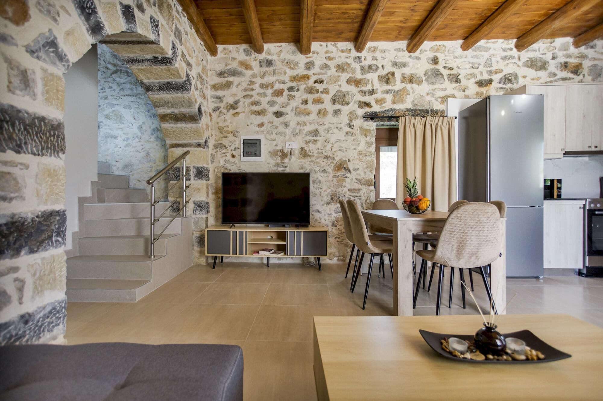 Un espace de vie aux murs en pierre, comprenant un téléviseur, une table à manger et des chaises.