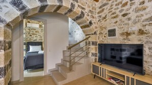 A cozy room with a stone wall, a staircase leading to a bedroom, and a TV on a wooden stand. - Stoney Villa Koxari By Estia (Hersonissos)